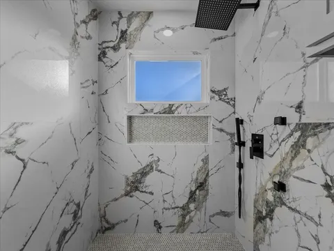 Walk-in shower with marble walls, rain showerhead, and built-in niche
